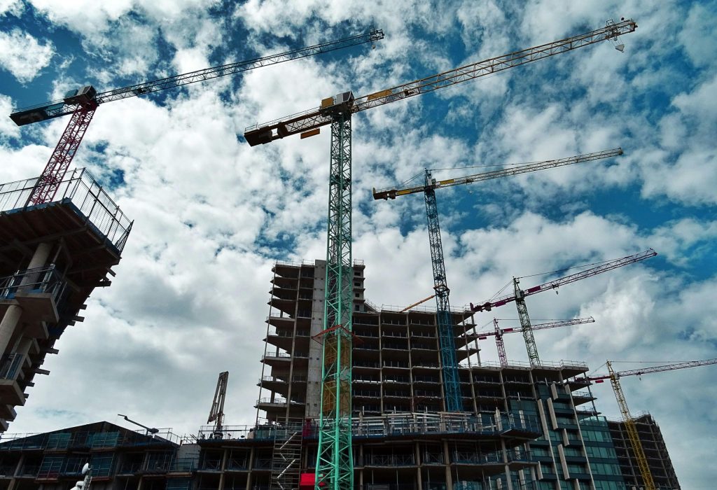 Urban construction site with numerous cranes framing rising skyscrapers against a blue sky.